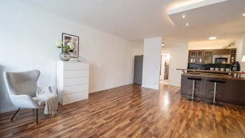 Heller offener Wohnbereich mit Holzboden, integrierter Bar und moderner Deckenbeleuchtung.