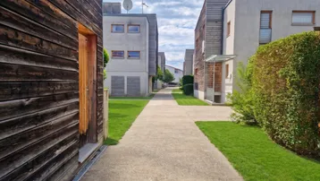 Weg zwischen modernen Reihenhäusern mit Holzfassaden und gepflegten Hecken.