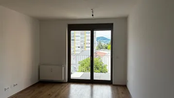 Heller Wohnraum mit Laminatboden und Zugang zu einem Balkon, der einen weiten Blick bietet.
