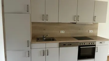 Moderne Einbauküche in hellem Grau mit Holzoptik-Arbeitsplatte und integrierten Geräten.