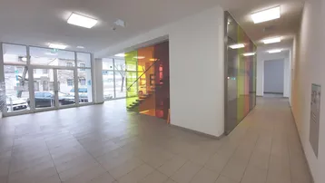 Moderner Eingangsbereich mit großen Fenstern, Fliesenboden und einer farbigen Glaswand um die Treppe.
