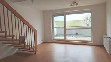 Helles Wohnzimmer mit Holztreppe, Laminatboden und Zugang zu einer Terrasse mit Blick ins Grüne.