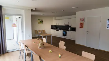 Großer Gemeinschaftsraum mit Essbereichen und integrierter Küchenzeile, ideal für soziale Aktivitäten.