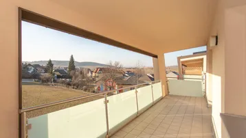 Heller Balkon mit Fliesenboden und Glasgeländer, bietet einen weiten Blick über die umliegende Landschaft.