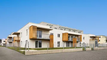 Modernes Mehrfamilienhaus mit Balkonen und schlichter Architektur unter blauem Himmel.