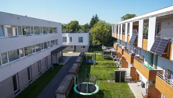 Blick von oben auf eine Wohnanlage mit mehreren Gebäuden, Grünflächen und Balkonen mit Solarpaneelen.