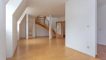 Heller, leerer Wohnbereich mit Holztreppe und Parkettboden, bereit zur individuellen Gestaltung.