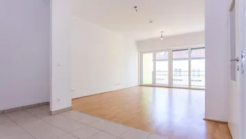 Heller, leerer Wohnbereich mit Parkettboden und Zugang zu einem Balkon.