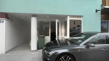 Die moderne Fassade des Gebäudes in Mintgrün mit Eingangsbereich und einem geparkten Auto davor.