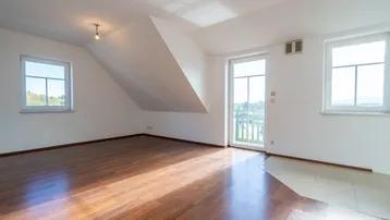 Helles Zimmer im Dachgeschoss mit Holzboden, Zugang zum Balkon und schrägen Wänden.