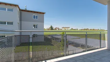 Balkon mit weitem Blick über grüne Felder und ländliche Umgebung unter blauem Himmel.