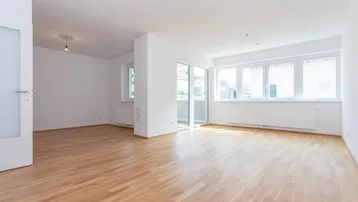 Helles, leeres Wohnzimmer mit Parkettboden und Zugang zu einem Balkon, ideal für individuelle Gestaltung.