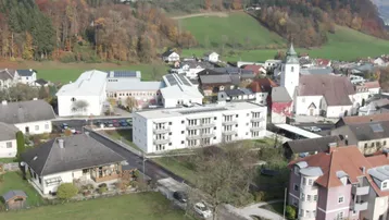 Luftaufnahme einer ländlichen Ortschaft mit einem modernen Wohngebäude im Zentrum und grüner Umgebung.