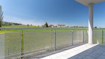 Heller Balkon mit Fliesenboden und weitem Blick ins Grüne unter blauem Himmel.