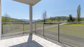 Geräumiger Balkon mit Fliesenboden und weitem Blick über grüne Hügel und Berge.
