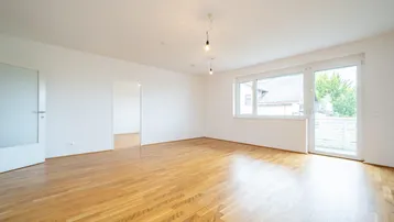 Helles, leeres Zimmer mit Parkettboden und Zugang zu einem Balkon, ideal als Wohnbereich.