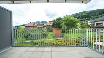 Geräumiger Balkon mit Fliesenboden und Blick auf den Garten sowie die umliegende Landschaft.