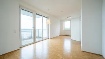 Helles Zimmer mit Parkettboden und großen Schiebetüren zum Balkon, bietet viel Tageslicht.