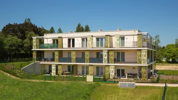 Modernes Mehrfamilienhaus mit Balkonen und grüner Umgebung unter blauem Himmel.