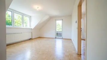 Helles Zimmer im Dachgeschoss mit Parkettboden, Schrägdecke und Zugang zu einem kleinen Balkon.