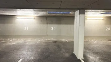 Tiefgaragenstellplätze mit Betonwänden und Decke, beleuchtet durch Leuchtstoffröhren.
