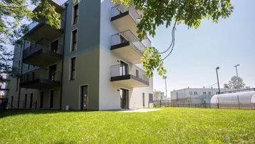 Modernes Mehrfamilienhaus mit Balkonen und einer gepflegten Rasenfläche im Vordergrund.