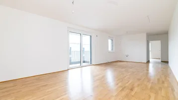 Helles, leeres Wohnzimmer mit Holzboden und Zugang zu einem Balkon.