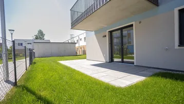Helle Terrasse mit direktem Zugang zum Rasen und Blick auf die umliegenden Gebäude.