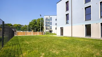 Moderne Wohngebäude mit hellblauer und beiger Fassade, umgeben von einer grünen Rasenfläche.