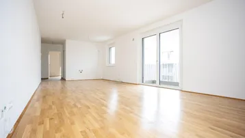 Helles, leeres Wohnzimmer mit neuem Parkettboden und Zugang zu einem Balkon.