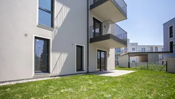 Neubau-Fassade mit Balkonen, Terrasse und Rasenfläche im Vordergrund, ideal für Erholung.