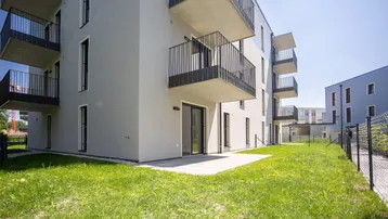 Moderne Wohnanlage mit Terrassenzugang und Grünfläche im Außenbereich unter blauem Himmel.