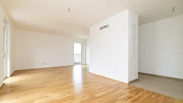 Helles, leeres Wohnzimmer mit hellem Parkettboden und Zugang zu einem Balkon.