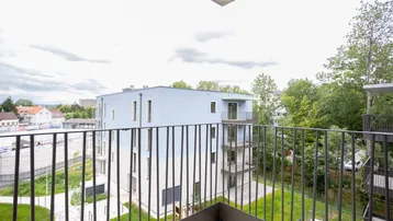 Blick vom Balkon auf ein modernes Wohngebäude und die umliegende grüne Landschaft.