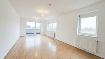 Helles, leeres Wohnzimmer mit Parkettboden und Zugang zu einem Balkon, ideal für individuelle Gestaltung.