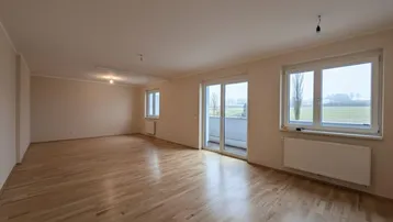 Geräumiges Wohnzimmer mit hellem Parkettboden und Zugang zum Balkon, bietet weite Aussicht.