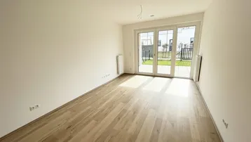 Helles Zimmer mit Holzboden und Zugang zu einem kleinen Gartenbereich.