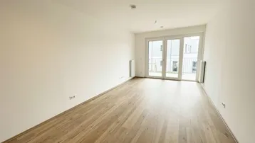 Helles, leeres Wohnzimmer mit neuem Laminatboden und Zugang zu einem Balkon.