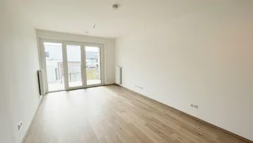 Helles Zimmer mit Holzboden und Zugang zu einem Balkon, ideal als Wohn- oder Schlafzimmer.