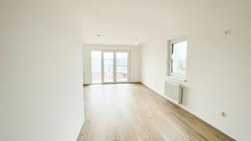 Helles, leeres Zimmer mit modernem Laminatboden und Zugang zu einem Balkon.