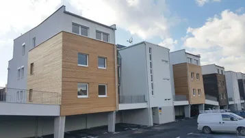 Moderne Wohnanlage mit Holzfassadenelementen und überdachten Parkplätzen im Erdgeschoss.