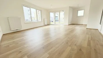Helles, leeres Wohnzimmer mit großen Fenstern, Laminatboden und Zugang zur Terrasse.