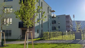 Modernes Mehrfamilienhaus mit hellgrüner Fassade, Balkonen und gepflegter Grünfläche im Vordergrund.