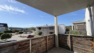 Blick vom Balkon mit Holzgeländer auf den Parkplatz und die umliegenden Gebäude.