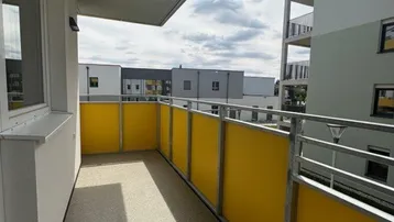 Langer Balkon mit gelben Sichtschutzelementen und Blick auf die umliegenden Wohngebäude.