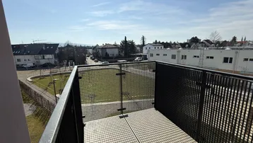 Heller Balkon mit Metallgeländer und Blick auf die umliegende Wohngegend unter blauem Himmel.