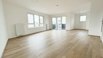 Helles Wohnzimmer mit neuem Parkettboden, großen Fenstern und direktem Zugang zum Balkon.