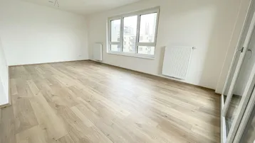 Helles, leeres Zimmer mit modernem Laminatboden und großen Fenstern, bereit zur individuellen Gestaltung.