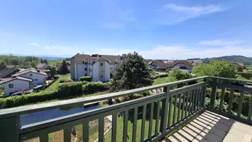 Geräumiger Balkon mit Fliesenboden und weitem Blick über die Landschaft und einen Teich.