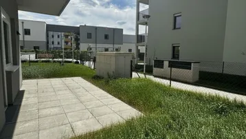 Terrasse mit Rasenfläche vor einem modernen Wohngebäude unter blauem Himmel.